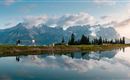 Eine beeindruckende Berglandschaft mit spiegelndem Wasser im Vordergrund. Der Himmel ist teilweise bewölkt, und Bäume umrahmen die Szene.