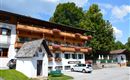 A traditional old building with a wooden balcony and colorful flowers. It is located in a quiet environment with trees and an asphalt road.
