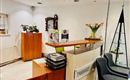 A friendly reception area in a dental practice. There is a wooden counter, chairs, and decorative plants.