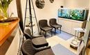 A cozy waiting area with modern black chairs and a green plant on the table. In the background, there is an aquarium with various fish.