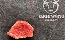Ein rohes Stück Wagyu-Fleisch auf einer dunklen Oberfläche. Daneben steht das Logo "Kaiser Wagyu" für höchste Qualität.