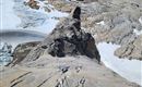 Ein Kletterer erklimmt eine steile Felswand mit Blick auf eine beeindruckende Berglandschaft. Schnee und Gletscher sind in der Umgebung sichtbar.