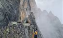 Ein Kletterer bestigt einen steilen, felsigen Gipfel mit Nebel in der Umgebung. Die dramatische Landschaft zeigt hohe Felsen und eine mystische Atmosphäre.