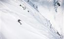Ein Skifahrer fährt über eine schneebedeckte Piste in den Bergen. Die Landschaft ist beeindruckend und die Umgebung wirkt unberührt.