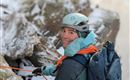 Eine Person beim Klettern in schneebedecktem Gelände. Sie trägt einen Helm und Rucksack und hält Seile in der Hand.