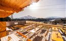 Eine sonnige Terrasse mit Holztischen und Bänken bietet einen Blick auf die Berge. Im Hintergrund ist eine klare, blaue Himmelslandschaft zu sehen.