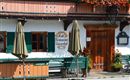 A traditional restaurant with an inviting entrance door and blooming plants. The green shutters and sun umbrellas give the place a cozy charm.