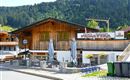 A cozy pizzeria with a wooden facade and outdoor terrace. Surrounded by green mountains and a quiet street.