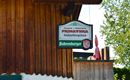 A restaurant sign with the name "Primavera" for wood-fired pizza. The background features wooden cladding and green trees.
