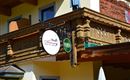 A traditional building with a wooden balcony. In front hang two signs, one with the name "Alpenblick" and the other with a reference to beer.