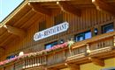 A traditional wooden building with a sign that shows "Cafe - RESTAURANT". Colorful flowers are blooming on the balcony and the windows are small and inviting.
