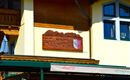 A restaurant named "Alexandra" is indicated by a wooden sign. In the background, parts of a yellow building and windows can be seen.