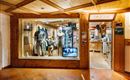 Een winkel met houten bekleding en een etalage, waarin kleding op manieken wordt gepresenteerd. Op de achtergrond zijn andere producten en een receptiebalie te zien.