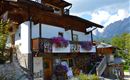 A charming wooden house with a balcony full of flowers. In the background, there are mountains and a clear sky.