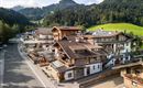 A picturesque mountain landscape with traditional wooden buildings. The surroundings are green and tranquil, with a road that runs through the village.