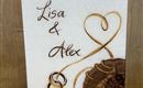 Eine dekorative Hochzeitskerze mit den Namen "Lisa & Alex". Das Datum "03.10.2026" und ein Herzsymbol sind ebenfalls darauf verzeichnet.
