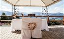 A beautifully decorated wedding table under a tent with a picturesque mountain landscape in the background. The chairs are adorned with white covers and a heart-shaped wreath.