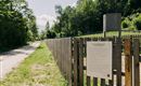 A gravel path leads through a green landscape with trees. An information sign stands at a wooden fence along the path.