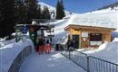 A ski lift station in a snow-covered area.  
People are standing in line to get on the lift.