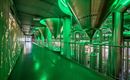 Een moderne binnenruimte met grote, groene opslagtanks en metalen leidingen. De vloer is groen en de ruimte heeft een industriële sfeer.