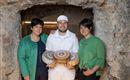 Drie personen staan in een historische kelder. Ze houden kaas in hun handen en glimlachen naar de camera.
