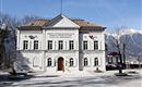 Ein historisches Gebäude mit klassischer Architektur und bunten Verzierungen. Im Hintergrund sind Bäume und ein klarer Himmel zu sehen.