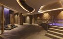 An elegant spa area with wooden paneling and soft lighting. A staircase leads to a water area with a relaxing atmosphere.