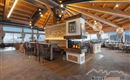 Eine moderne Restaurant-Umgebung mit Holzinterieur und großen Fenstern, die auf die Berge blicken. Der Raum ist einladend und hell, mit einer Bar und gemütlichen Sitzbereichen.