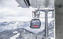 A cable car in the mountains on a snowy day. In the background, snow-covered mountains and a clear sky can be seen.