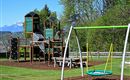 A playground with a slide and swings. In the background, there are green trees and mountains.