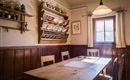 Ein gemütlicher Raum mit einem Holztisch und Stühlen. An der Wand sind Geschirr und Vorratsbehälter zu sehen, während ein Fenster natürliches Licht hereinfluten lässt.