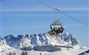 Een groep skiërs rijdt in een gondel over besneeuwde bergen. De heldere lucht en het indrukwekkende landschap creëren een winters sfeer.