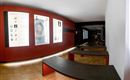 Ein moderner Innenraum mit roten Wänden und Ausstellungsplakaten. Flache Bänke laden zum Verweilen ein.