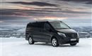 Ein schwarzer Mercedes-Van steht auf schneebedecktem Boden. Im Hintergrund ist eine weite, winterliche Landschaft mit einem farbenfrohen Himmel zu sehen.
