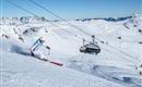A skier glides through the fresh snow in the mountains. In the background, a ski lift is visible.
