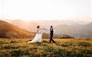 A bridal couple dances happily on a green meadow in the mountains. In the background, the setting sun glows.