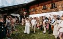 A bride and groom celebrate in front of a traditional wooden house. Surrounded by cheerful guests who cheer with flowers and confetti.