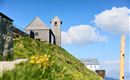 A picturesque mountain with two charming buildings. The sky is clear and blue, surrounded by gentle clouds.