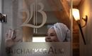 A woman with a towel on her head smiles behind a glass wall with the inscription "BuchackerAlm". Soft light illuminates the room, creating an inviting atmosphere.