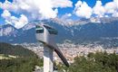 Ein modernes Aussichtsturm erhebt sich über der Stadt, umgeben von schönen Bergen und Bäumen. Ein strahlend blauer Himmel mit weißen Wolken vervollständigt die malerische Aussicht.