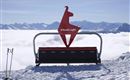 A ski lift station with a distinctive sign in the shape of a llama. In the background, snow-covered mountains and a sea of clouds can be seen.