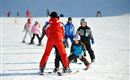 A ski school on a snowy slope with children in winter sports clothing. A teacher is helping the children with skiing.