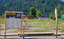 Ein Skillpark für Mountainbiker mit einem Informationsschild. Im Hintergrund sieht man die umliegenden Berge und einige Gebäude.