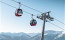 A cable car travels over snow-covered mountains. The sky is clear and blue.