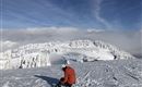 Een skiër zit op een met sneeuw bedekte bergtop. De lucht is helder en het landschap is omgeven door met sneeuw bedekte bomen.