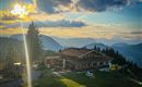 Eine charmante Berghütte umgeben von majestätischen Bergen. Die Sonne geht hinter den Gipfeln unter und taucht die Landschaft in warmes Licht.
