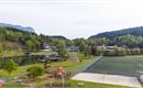 A quiet park with a playground and a large sports field. In the background, trees and mountains can be seen.