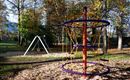 A beautiful playground with a climbing structure and swings. In the background, colorful trees can be seen.