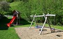 A beautiful playground with a slide and a swing. In the background, green trees can be seen.