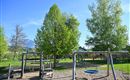 A beautiful playground with swings and a slide. Surrounded by green trees and clear sky.
